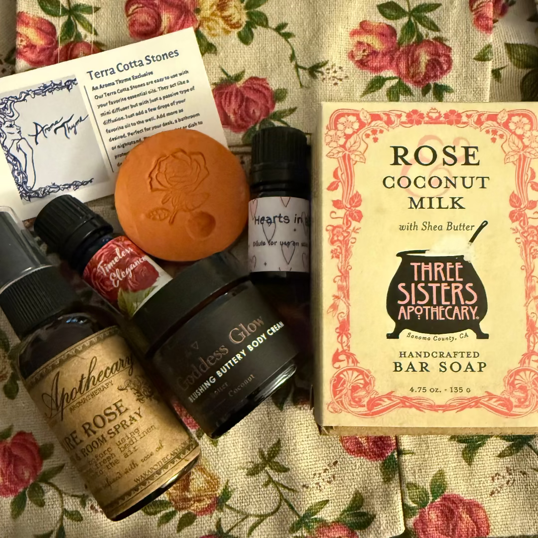 Collection of assorted aromatherapy products including soap, body cream, and oils on a floral fabric background.